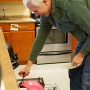 Male client is in the kitchen bending over and loading the dishwasher with dishes.