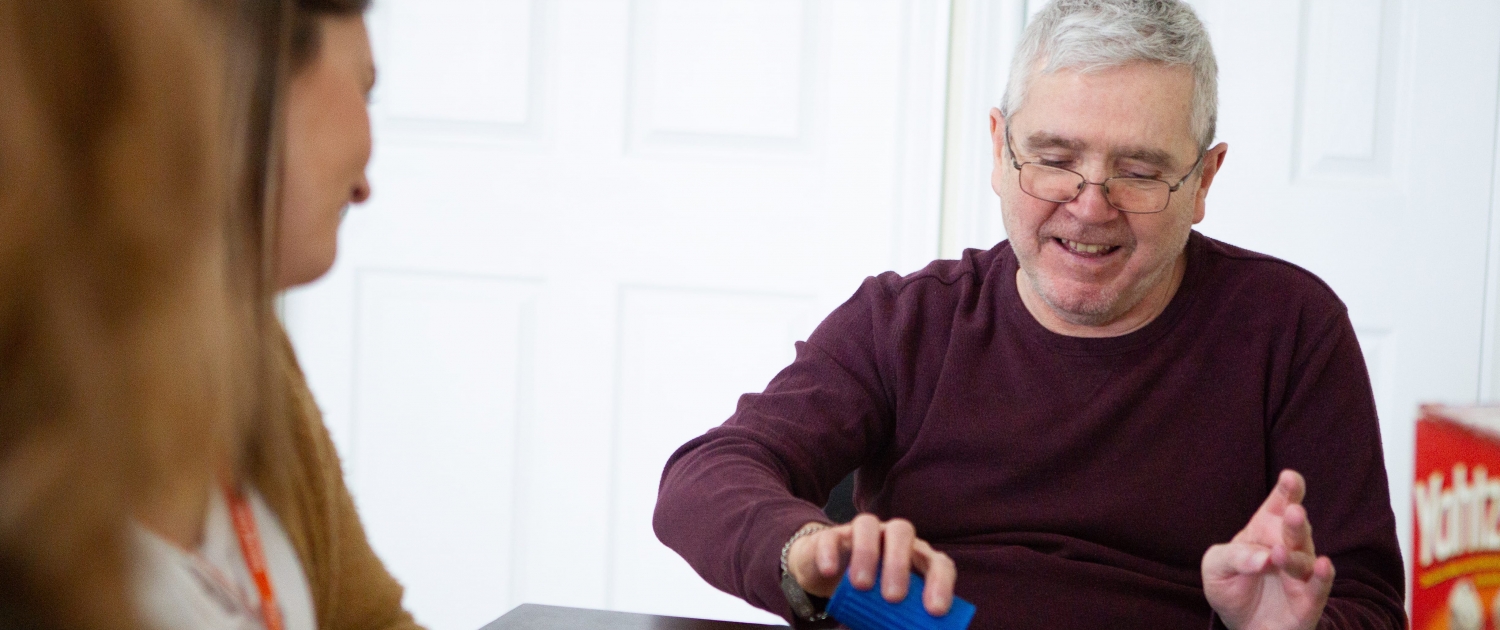 Male client empties out his cup of yahtzee dice onto the table while female staff looks on. They both are smiling.