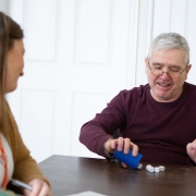 Male client empties out his cup of yahtzee dice onto the table while female staff looks on. They both are smiling.