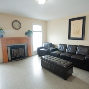 Beige living room with fire place between 2 windows on the left side. 2 brown lazy boy chairs, a sofa and an ottomon at the back of the room with a large picture of flowers hanging over the sofa.