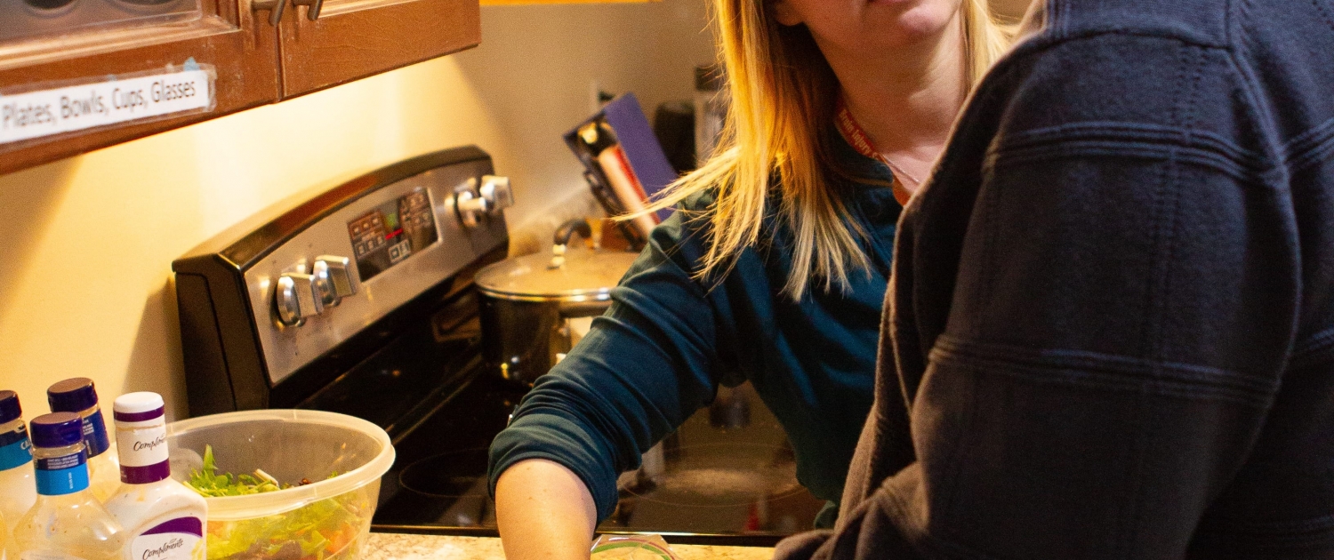 Male client and female staff are standing side by side at a kitchen counter working together preparing food.