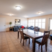 Living area with dining table and chairs. Seating and conversational area with couches is in the corner by large bright windows.