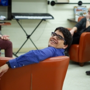 Male client looking relaxed in a big large orange armchair has his head turned around to smile at the camera. There is another orange armchair with a client sitting in the room in the background.