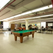 Large, spacious and bright games room. Pool table in the middle of the room has lots of open space around it. A few tables with chairs are set up in the background to accommodate other client activities.