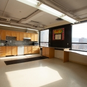 Large and spacious communal full kitchen for Group Services. Open floor space is available in the middle of the room; wooden cabinetry including a diswasher span the back wall. 2 large windows provide a lot of natural light into the space.