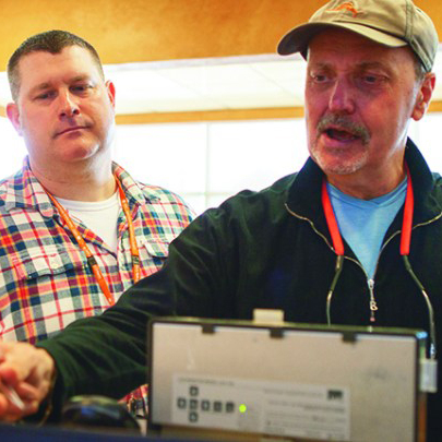 Non-verbal male client is ordering a coffee with communication cue cards at a local coffee shop. He is handing the information card to the staff behind the counter while the male staff stands behind watching and supporting.