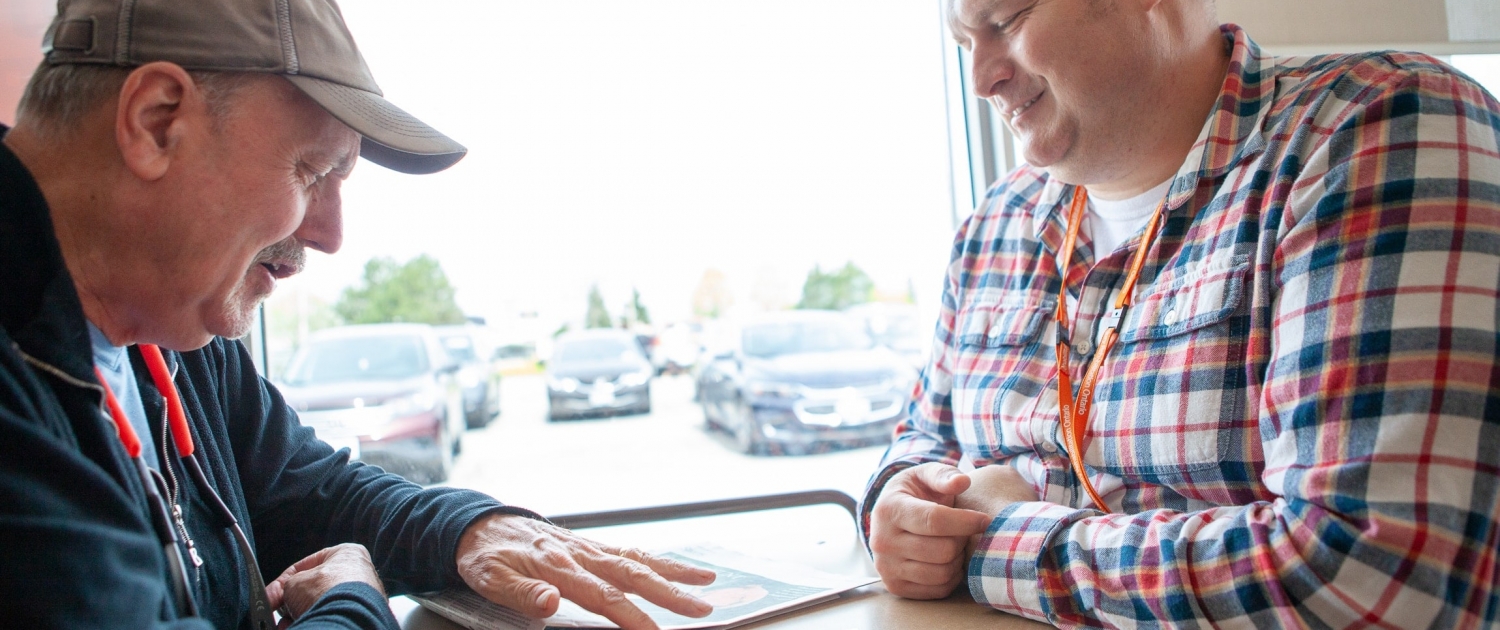 Non-verbal male client is sitting across the table from a male staff member at a local coffee shop. The client is working on his communication skills while the male staff smiles and watches.