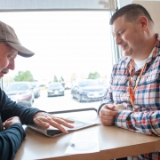 Non-verbal male client is sitting across the table from a male staff member at a local coffee shop. The client is working on his communication skills while the male staff smiles and watches.