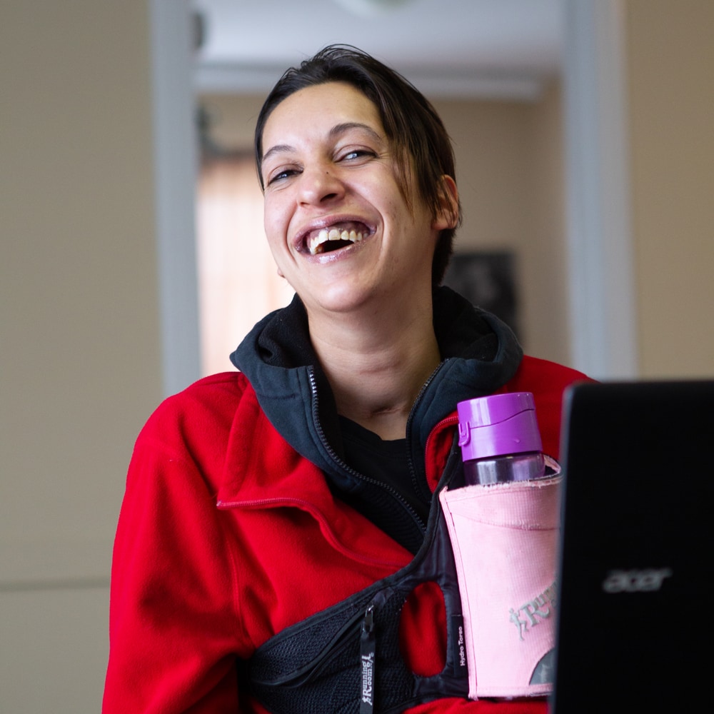 Young female client looks very happy and has a big wide smile on her face while sitting in front of a comuputer working on skill development.